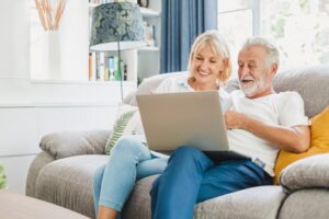 A man and woman sitting on the couch looking at a laptop.