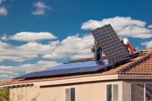 A man standing on top of a roof with a solar panel.